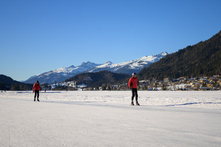Weissensee, Austria - February 8, 2022: Lake Weissensee (Austria) on a cold sunny day in winter, people skatingのeditorial素材