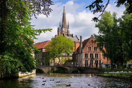 Bruges, Belgium-July 4, 2022: A canal in Bruges with a church in the distance, summer, parkのeditorial素材
