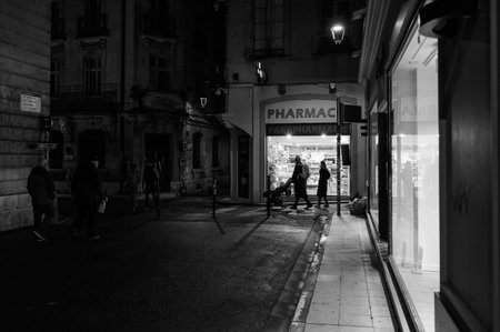 Arles, France - March 7, 2023: Empty street in the center of Arles (France) in the night, black and white, people in front of Pharmacyのeditorial素材