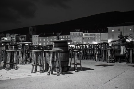 Cres, Croatia - October 24, 2022: The harbor of Cres in the night, empty chairs of a bar, black and...
