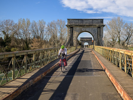 Arles, France - March 12, 2023: Cyclist crossing the Pont De Fourques suspension bridge on a sunny day in springtimeのeditorial素材