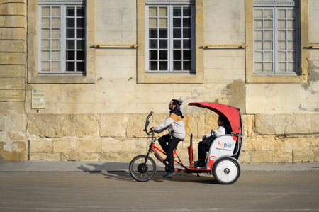 Arles, France - March 1, 2023: Red bicycle taxi in the city on a sunny day in winter, in front of an...