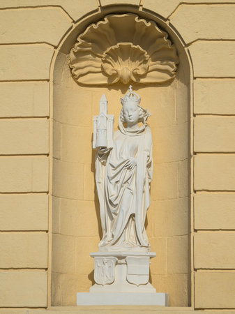 Saint Agnes white stone statue holding a church against yellow wall of Klosterneuburg Abbey on sunny dayの写真素材