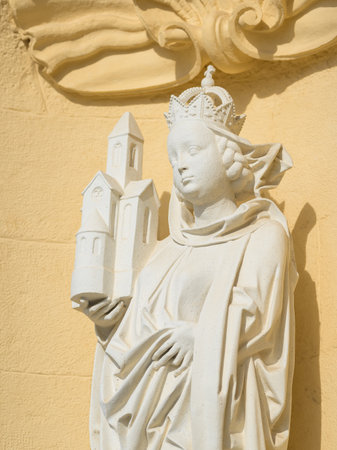 White stone statue of Saint Agnes holding a church against yellow wall of Klosterneuburg Abbey on sunny dayの写真素材