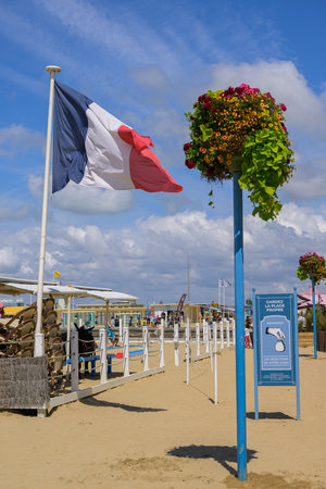 Trouville-sur-Mer, France - July 26, 2022: A French flag stands on the sand beach under a sunny summer sky creating a coastal scene.のeditorial素材
