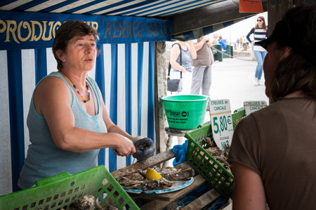 Cancale, France - August 13, 2018: A street stall sells oysters in Cancale France on a cloudy summer day with vendor talking to customers.のeditorial素材
