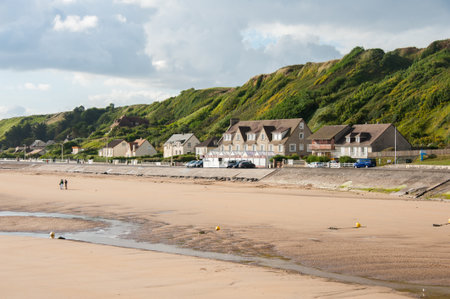 Vierville-sur-Mer, France - August 10, 2016: A sand beach lies at Omaha Beach with houses behind under a cloudy summer sky.のeditorial素材