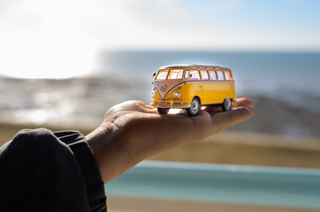 Ault, France - July 15, 2022: Hand holding miniature yellow VW bus model against clear sky on summer dayのeditorial素材