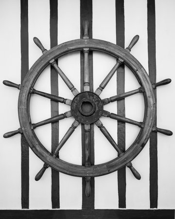 A ship steering wheel hangs on a wall in Trouville-sur-Mer France captured in black and white creating a nautical atmosphere.の写真素材