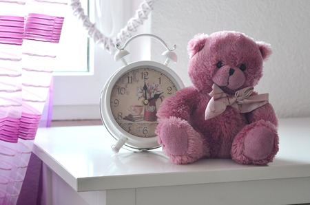 Romantic still life with alarm clock and pink plushy teddy bear in the foreground a pink curtain and heart in the backgroundの写真素材