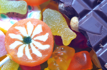 Macro detail of lollipop, gummy bears, chocolate and sour candy on colored smarties backgroundの写真素材