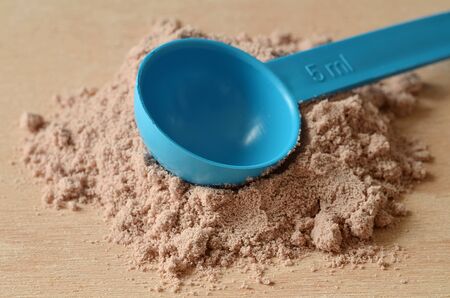 Close-up detail of blue scoop in heap of chocolate protein powder on wooden deskの写真素材