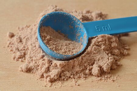 Close-up detail of blue scoop in heap of chocolate protein powder on wooden deskの写真素材