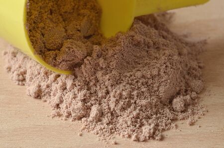 Close-up detail of chocolate protein powder spilled from yellow scoop on wooden deskの写真素材