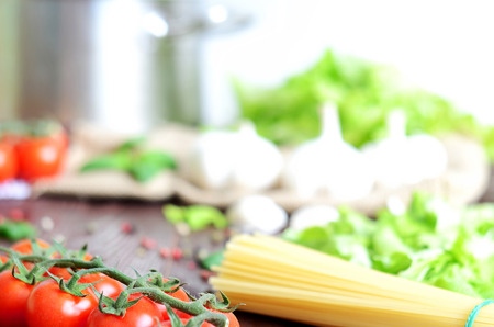 Cherry tomatoes, garlic, spaghetti and salad on wooden table and stainless steel pot in backgroundの写真素材