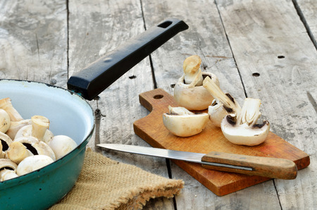 Slicing champignons on a wooden chopping board, knife, old pan and sackcloth on wooden tableの写真素材