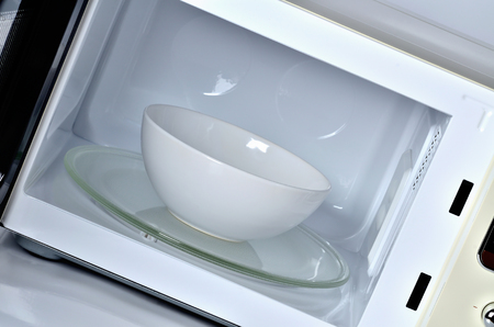 Inside of the microwave oven with clean empty white bowlの写真素材
