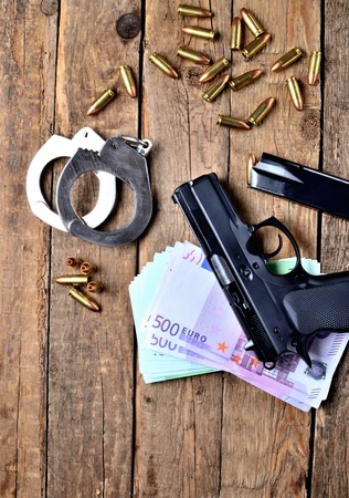 View from above of 9mm pistol gun - handgun, handcuffs, special police hollow-point expanding bullets, euro banknotes and magazine on old wooden tableの写真素材