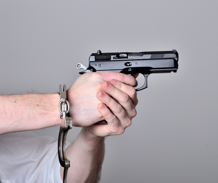 Hands with handcuffs pointing a pistol gun isolatedの写真素材