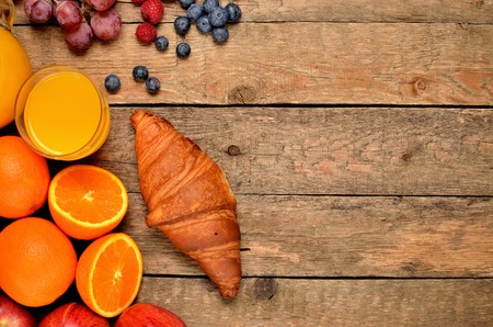 Croissant, oranges, blueberries, raspberries, apples - sweet breakfast on wooden table - view from aboveの写真素材