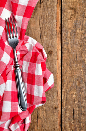 Fork on red checkered tablecloth right frame on vintage wooden table background - view from above - vertical photoの写真素材