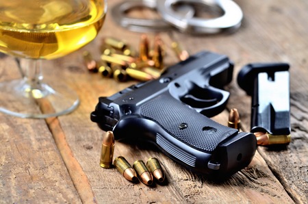 Glass of whiskey, 9mm pistol, handcuffs, bullets and magazine on old wooden tableの写真素材