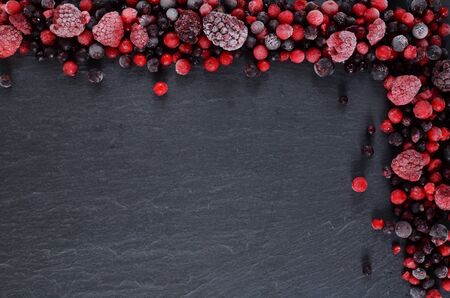 Frozen berries fruits in the upper right cornern on slate slab. Mix of raspberries, blueberries. and red currants. Top view. Copyspace.の写真素材
