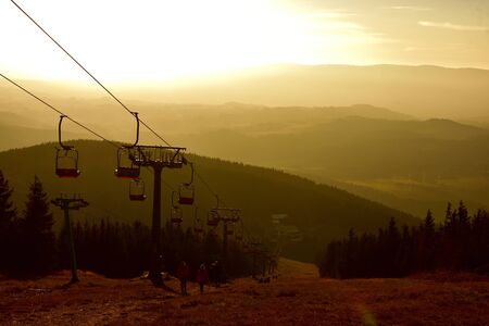 People walks under ski chair lift in the Jeseniky mountains at sunset.