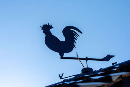 Silhouette of a tin rooster on roof showing the sides of the worldの写真素材