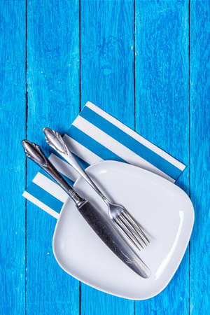 Background with empty squared white ceramic plate and silver cutlery on blue wooden boards. Copyspace. Vertical photo.の写真素材