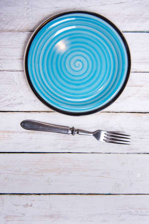 Top view background with empty blue ceramic plate, antique silver cutlery on vintage weathered white wooden boards. Copyspace. Vertical photo.の写真素材