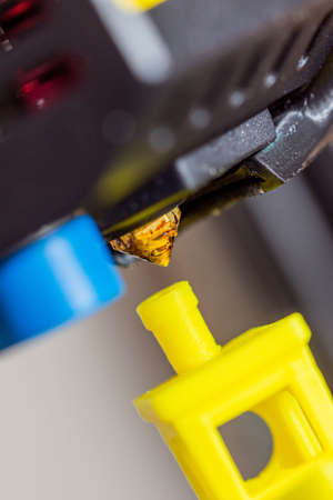Very close-up detail of 3D printer printerhead with hotend and fan printing yellow ship from ABS...