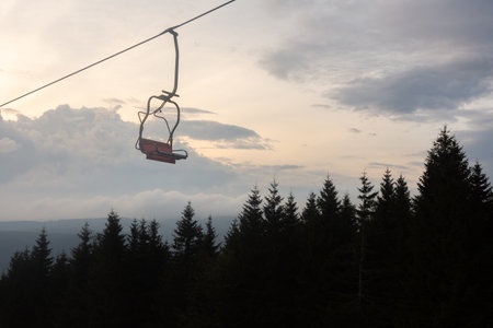 Chair lift in foreground, forrest and cloudy sky in background at evening.の写真素材