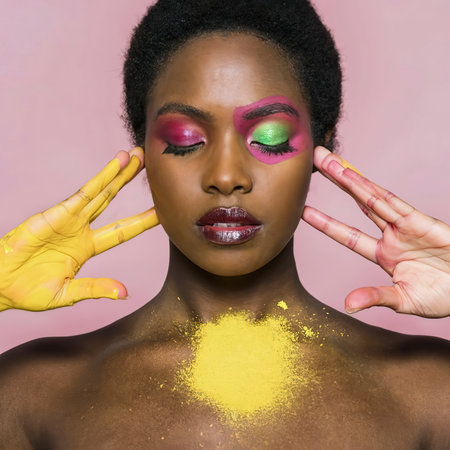 Black woman posing with pink and yellow powderの素材