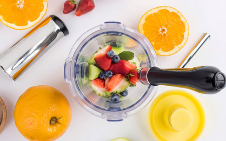 Black electric hand blender and accessories with sliced fruits on a white backgroundの素材