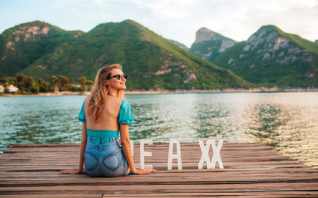 Amazing caucasian girl sitting at a pier on a resort next to inscription RELAXの素材