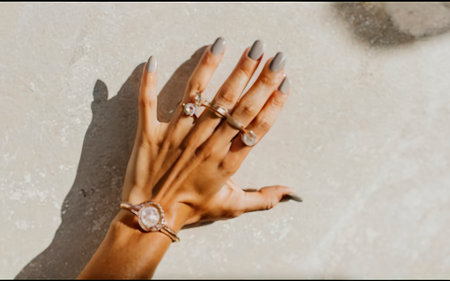 Aesthetic female hand with a light manicure and jewellery. Light sunny background with strong shadowsの素材