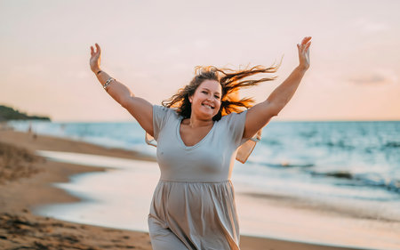 Happy woman on the beach with her arms outstretched enjoying the sunsetの素材