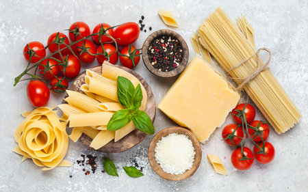 Pasta ingredients on white kitchen table. Raw Pasta, parmesan, olive oil, spices, tomatoes and basil. Top view with copy spaceの素材