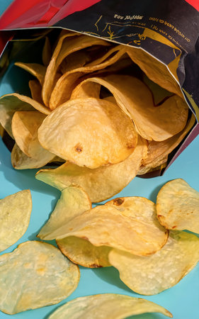 Fresh potato chips in an open package on a blue background.の素材