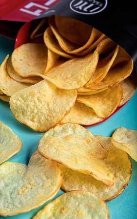 Fresh potato chips in an open package on a blue background.の素材