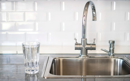 Glass of water stands on the countertop near the sink in the kitchenの素材