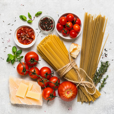 Pasta ingredients background. Pasta, tomato sauce, fresh tomatoes, parmesan, herbs and spices at white kitchen tableの素材