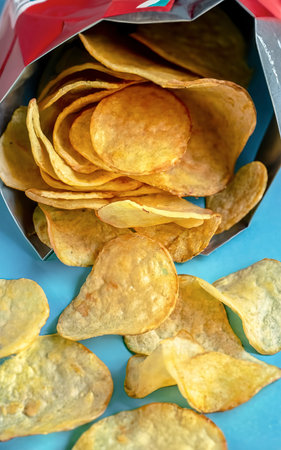 Fresh potato chips in an open package on a blue background.の素材