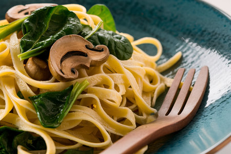 Fettuccine with spinach and mushrooms on a blue plateの素材