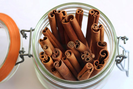 A close-up, overhead view of numerous cinnamon sticks tightly packed inside a clear glass jar. The...