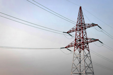 A towering lattice steel electricity pylon stands against a pale, hazy sky, with power lines stretching across the frame.の写真素材