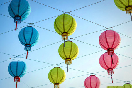 Numerous colorful paper lanterns in shades of blue, green, and pink hang suspended by strings against a bright, clear sky.の写真素材