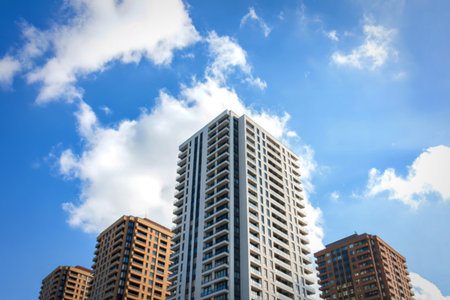 Towering modern apartment buildings with many windows rise against a backdrop of fluffy white clouds...