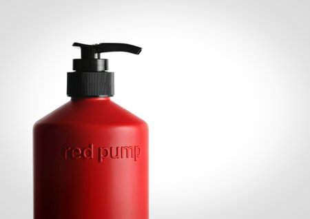 A close-up shot of a matte red bottle with a black pump dispenser, isolated on a clean white background.の写真素材